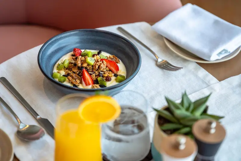 Un bol de yaourt aux fruits frais et un verre de jus d'orange sur une table.