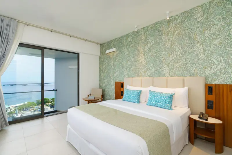 Chambre lumineuse avec un grand lit et vue sur la mer.