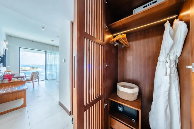 Une armoire ouverte dans une chambre lumineuse donne sur un espace de vie avec vue sur la mer.