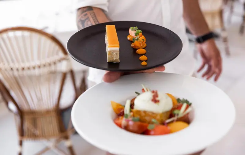 Un serveur présente un plat raffiné sur une table en terrasse.