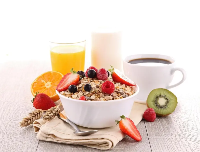 Un bol de céréales aux fruits frais et un jus d'orange sont présentés sur une table en bois.