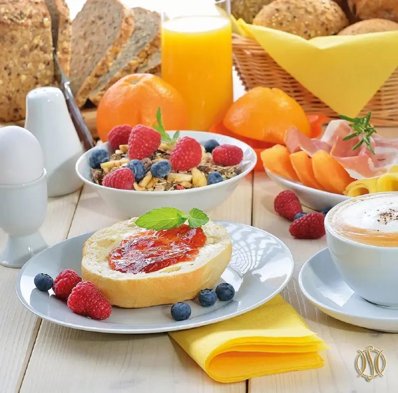Une table présente un assortiment de viennoiseries, de fruits frais, de céréales et de boissons.