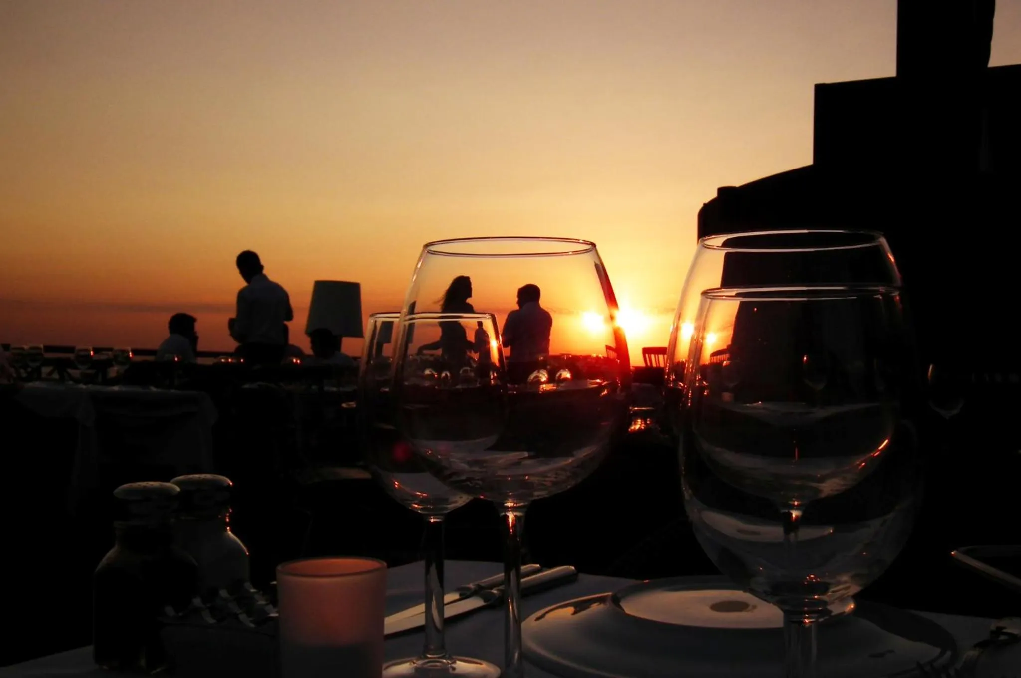 Des verres à vin et des assiettes sont disposés sur une table en contre-jour d'un coucher de soleil.