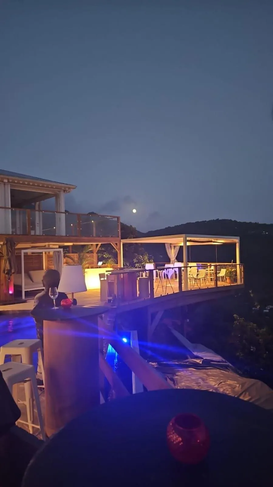 Terrasse lumineuse avec tables et chaises donnant sur un paysage nocturne.