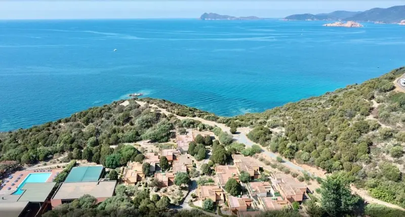 Vue aérienne d'un complexe hôtelier en bord de mer avec piscine et végétation luxuriante.