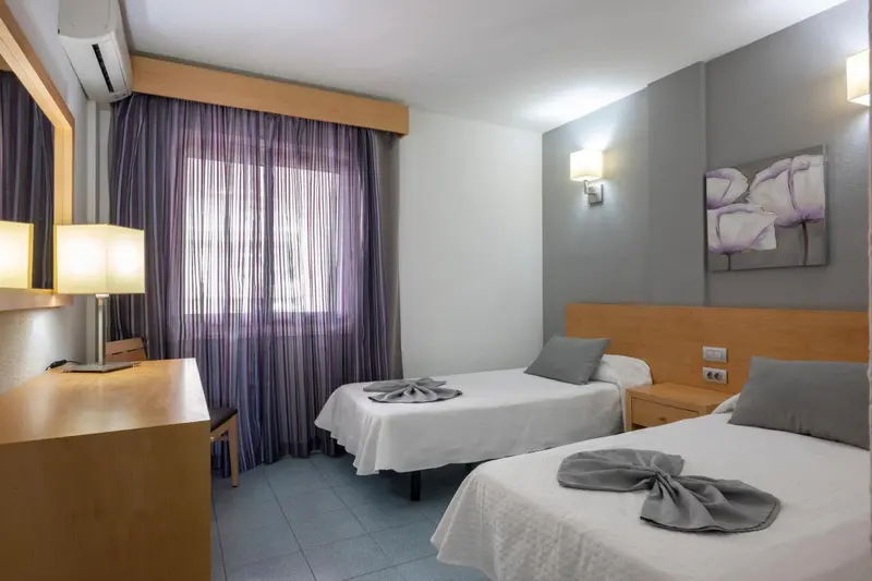 Chambre lumineuse avec deux lits simples et un bureau.