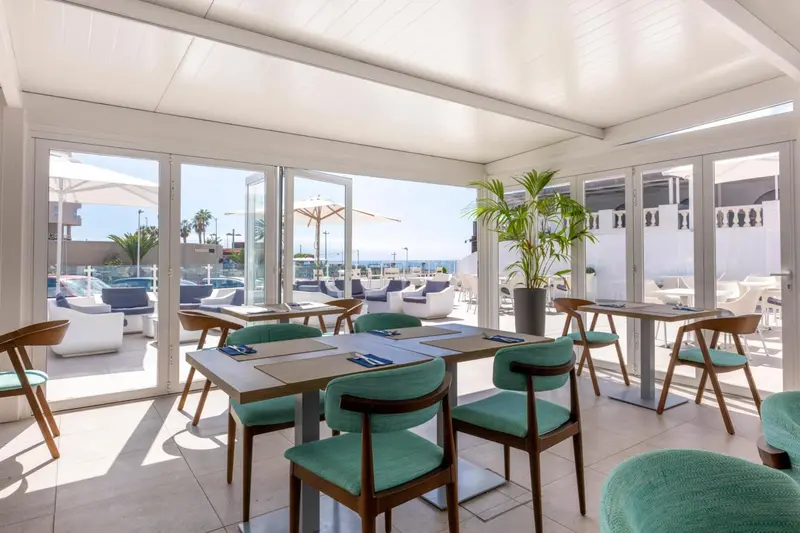 Une salle à manger lumineuse avec des tables dressées et vue sur une terrasse ensoleillée.
