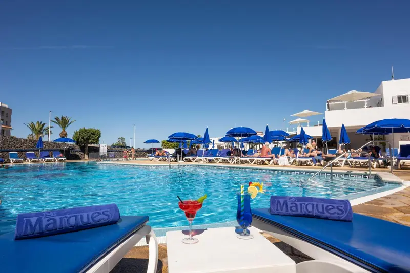 Deux cocktails colorés reposent sur des tables basses au bord d'une piscine ensoleillée.
