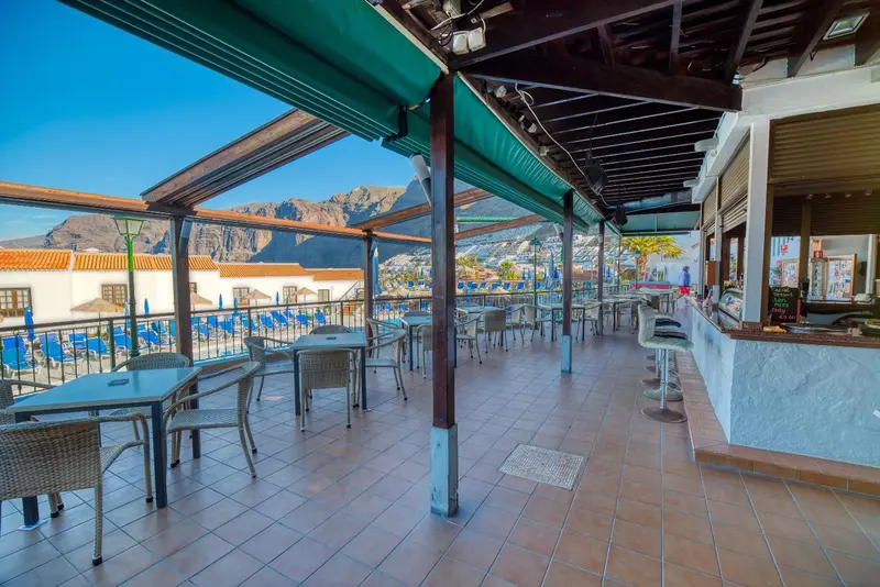 Terrasse ombragée avec tables et comptoir de bar en extérieur.
