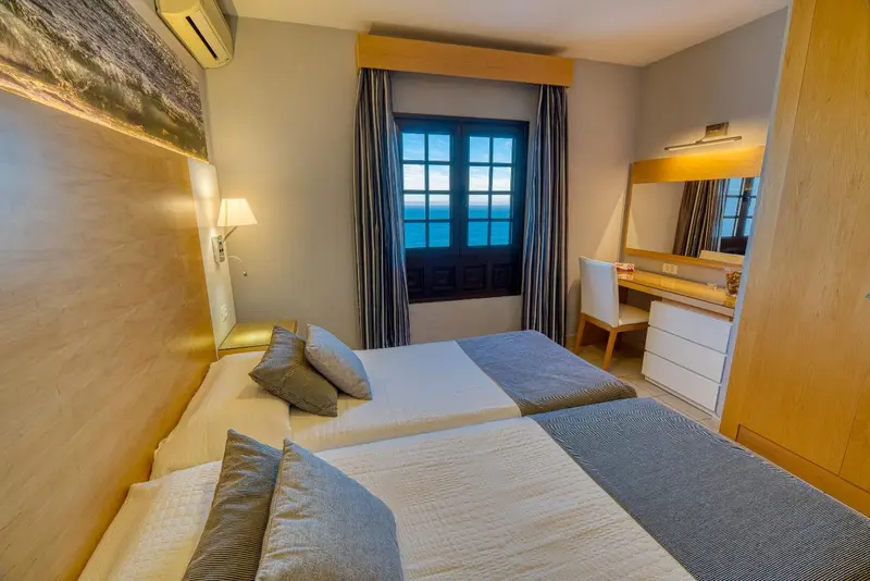 Une chambre lumineuse avec un grand lit et une coiffeuse près de la fenêtre.
