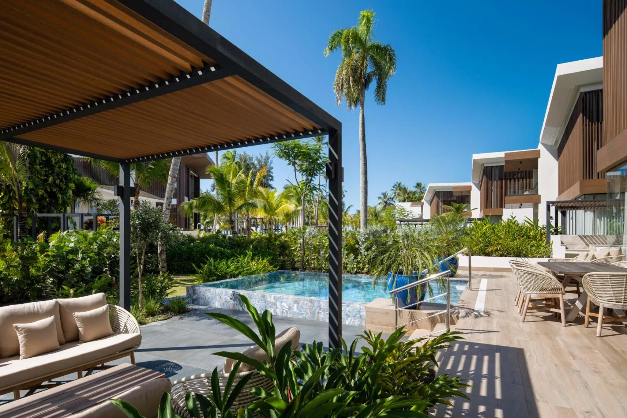 Terrasse ombragée avec salon et piscine au premier plan.