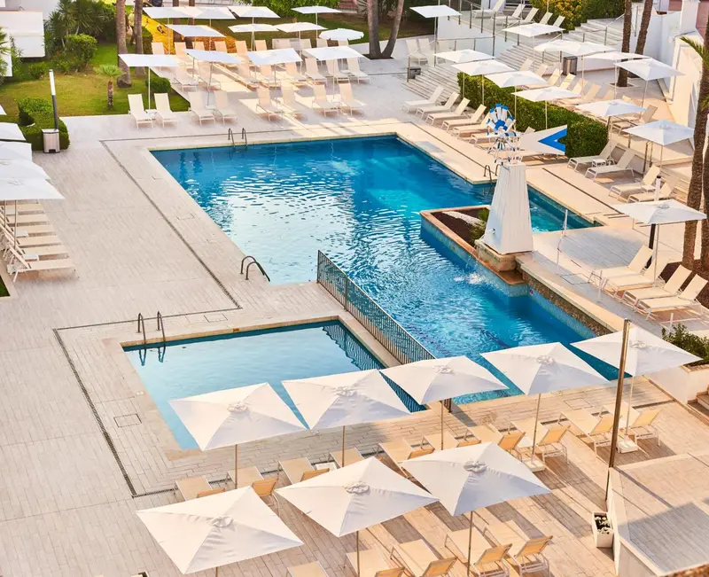 Vue aérienne d'une piscine rectangulaire entourée de transats blancs sous des parasols.