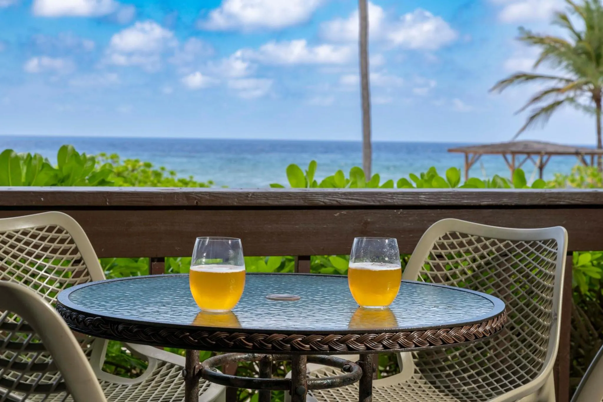 Deux verres de bière sur une table ronde en osier sur une terrasse ensoleillée avec vue sur la mer.