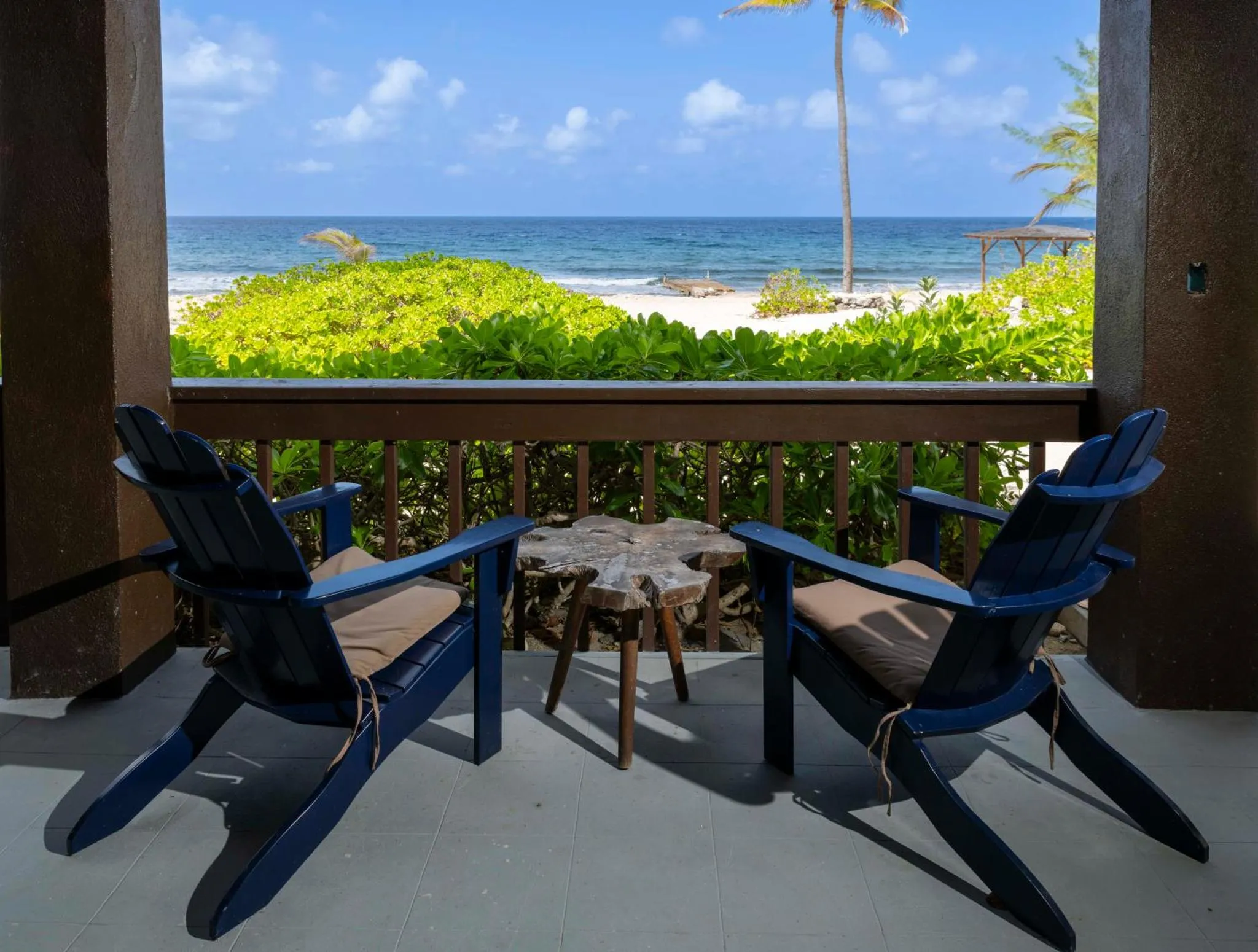 Deux fauteuils bleus et une table basse en bois ornent une terrasse ombragée avec vue sur la mer.