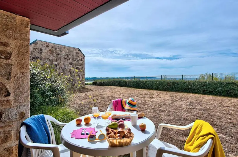 Une table ronde est dressée avec un petit-déjeuner sur une terrasse.