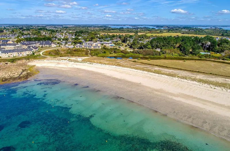 Vue aérienne d'une plage de sable fin bordée d'une eau turquoise et d'une côte rocheuse.