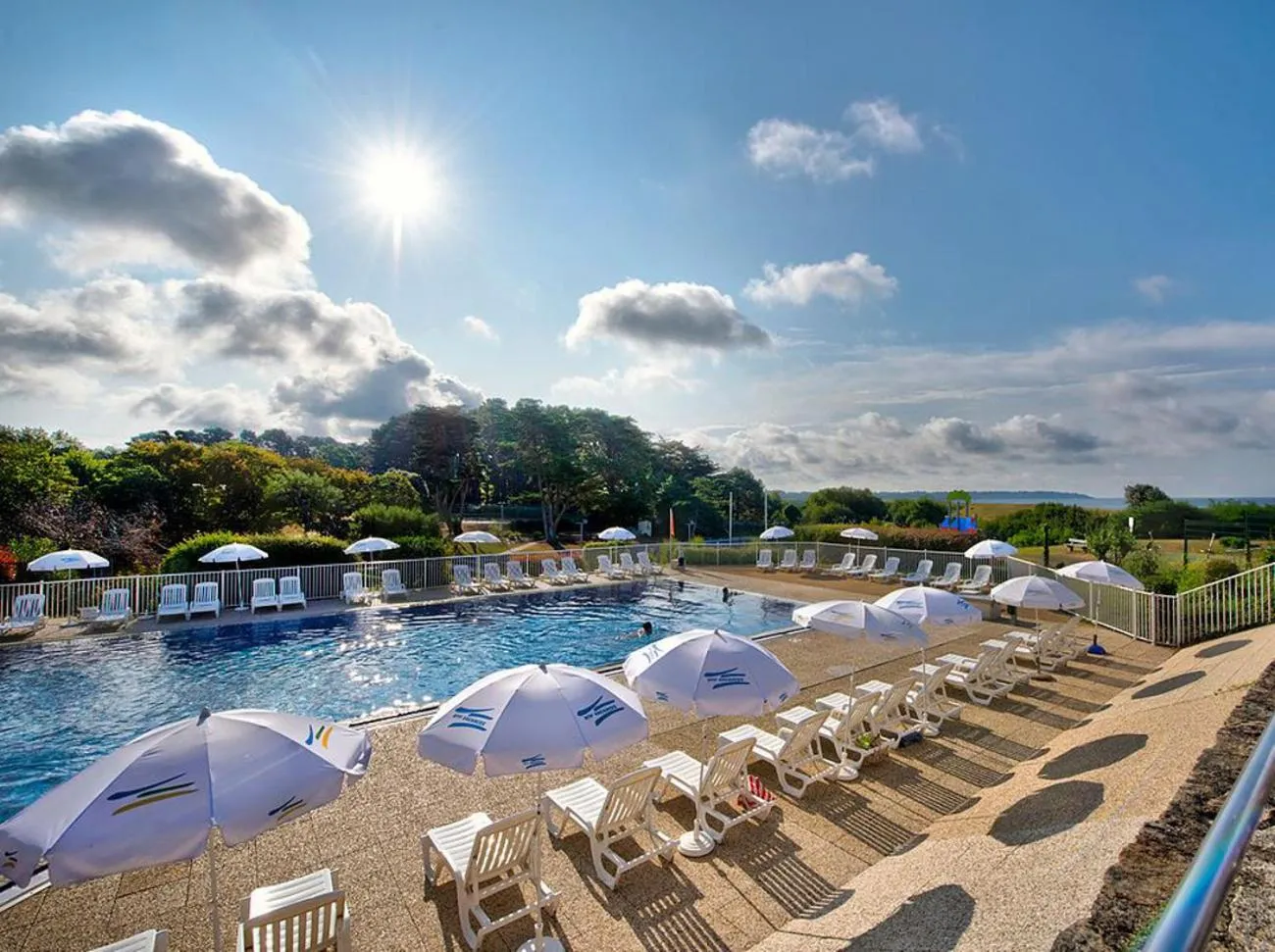 Une piscine ensoleillée avec des transats et des parasols blancs.