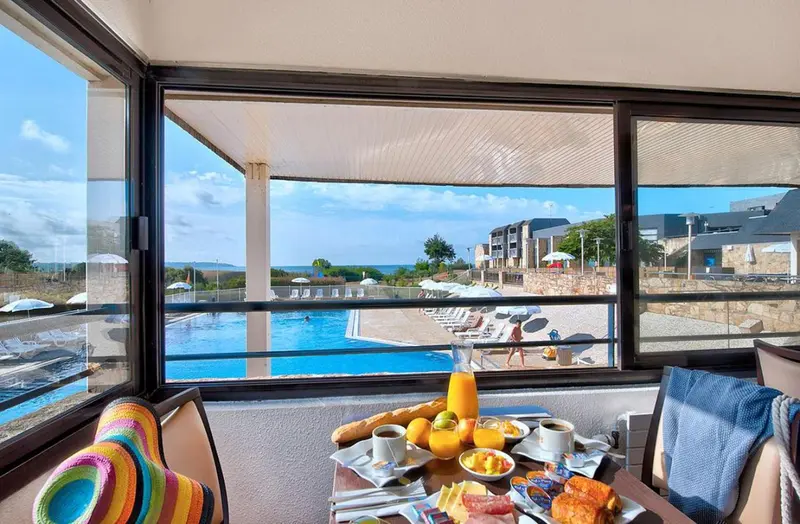 Une table est dressée avec un petit-déjeuner face à une piscine et à la mer.