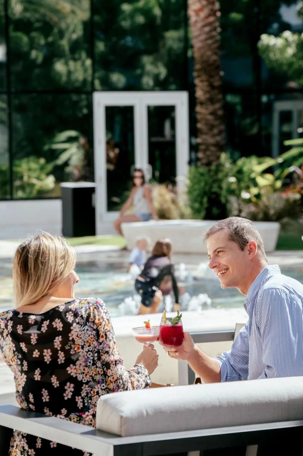 Un couple discute autour de boissons colorées près d'une piscine ensoleillée.