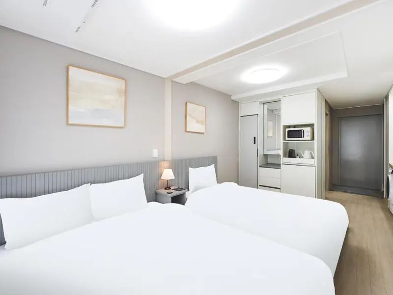 Chambre lumineuse avec deux lits simples et une kitchenette.