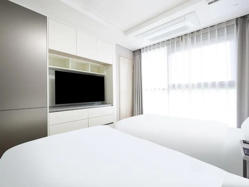 Une chambre lumineuse avec deux lits simples et un meuble télévision.