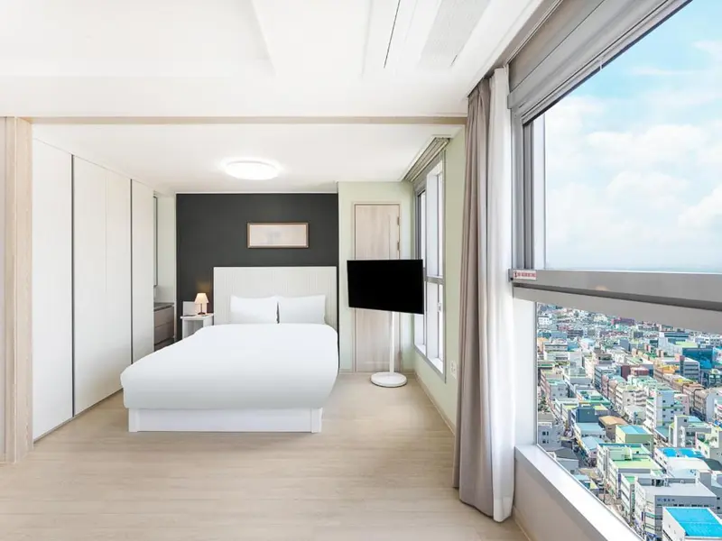 Chambre lumineuse avec un grand lit et une vue sur la ville.