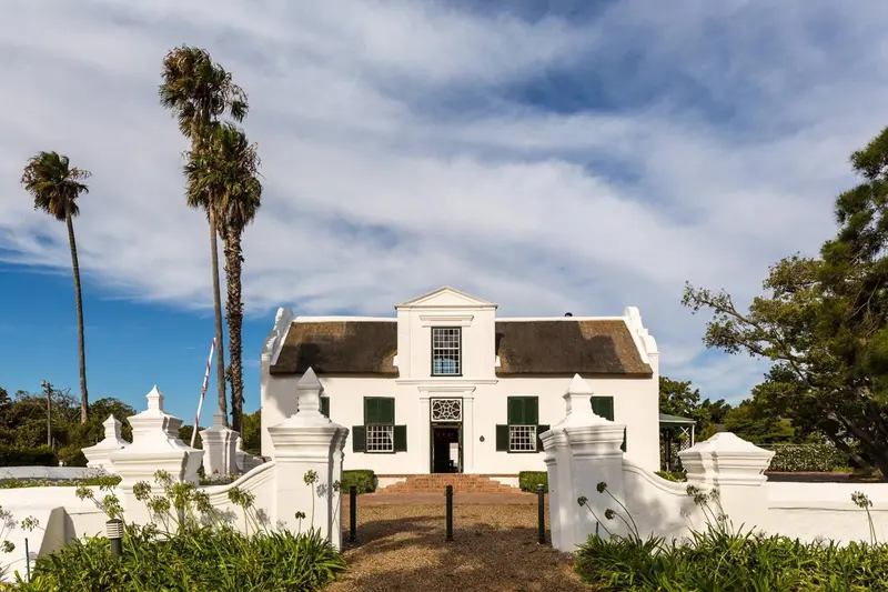Façade d'un bâtiment blanc à toit de chaume avec un jardin soigné.