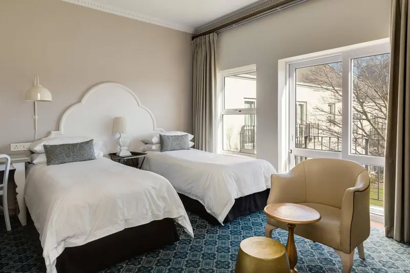 Une chambre lumineuse avec deux lits simples et un fauteuil.