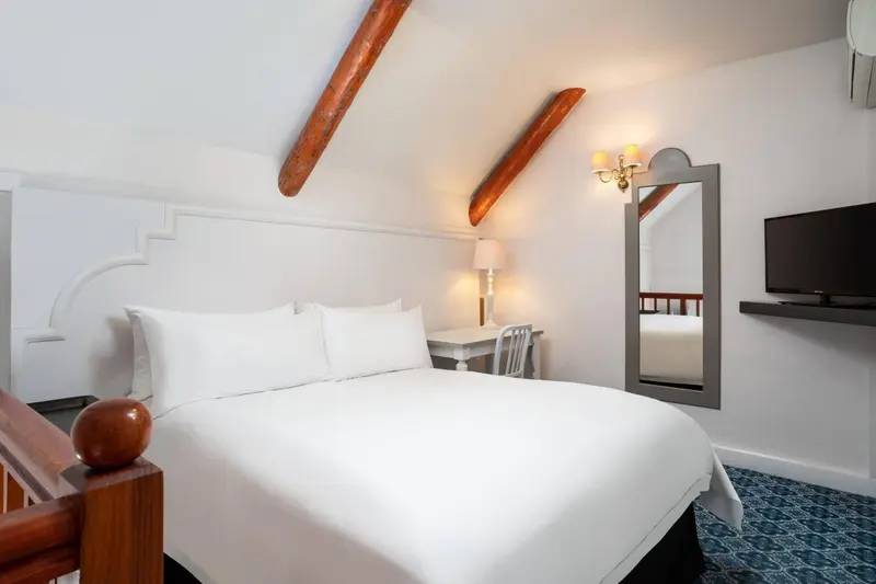 Une chambre lumineuse avec un lit blanc et un miroir décoratif.