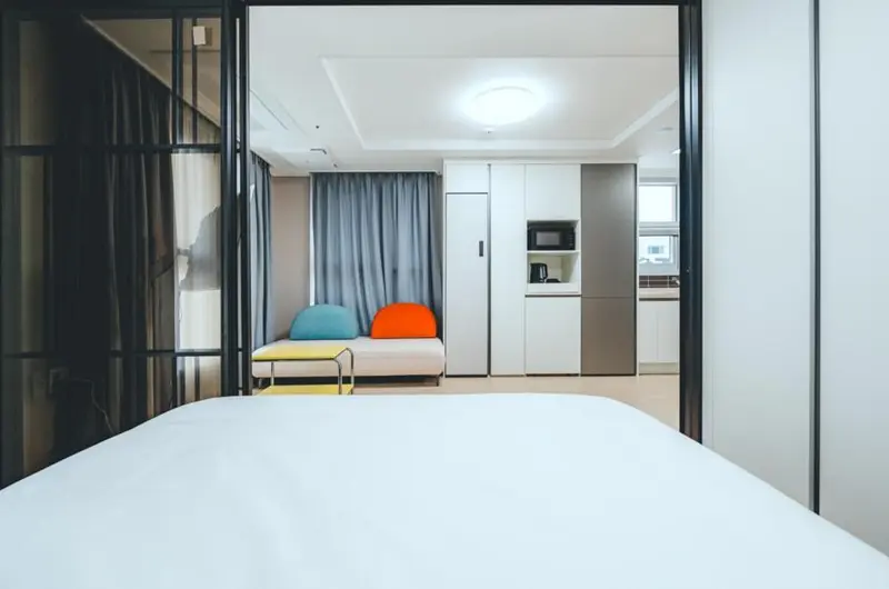 Une chambre lumineuse s'ouvre sur un espace de vie avec canapé et cuisine.