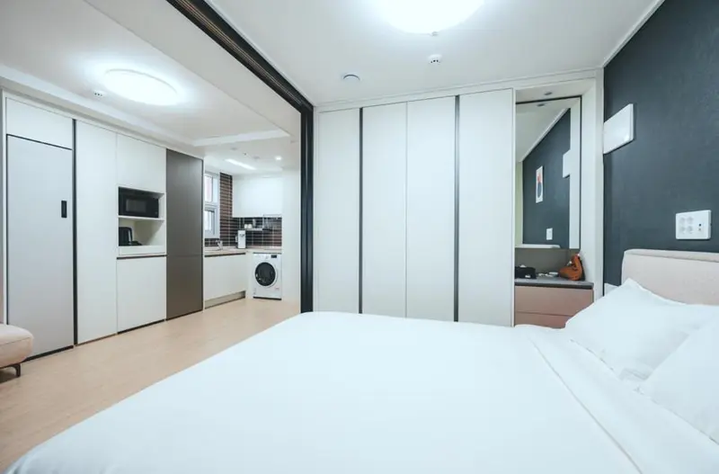 Une chambre lumineuse avec un lit fait et un espace cuisine.
