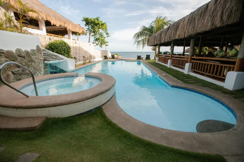 Une piscine rectangulaire avec un jacuzzi intégré, entourée d'une végétation luxuriante et d'une structure couverte.