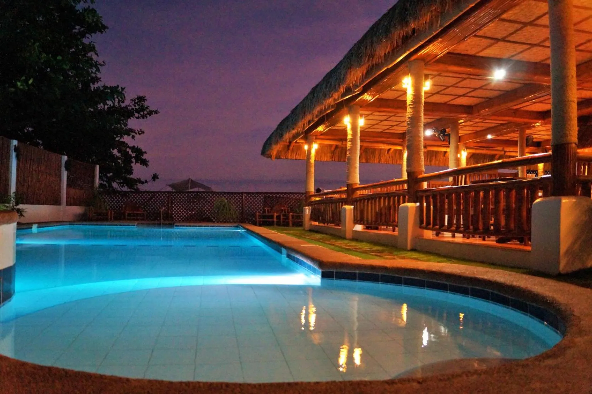 Une piscine illuminée jouxte un bar en plein air avec une vue sur la mer.