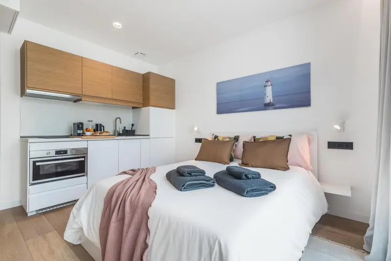 Une chambre lumineuse avec un lit fait et une kitchenette équipée.