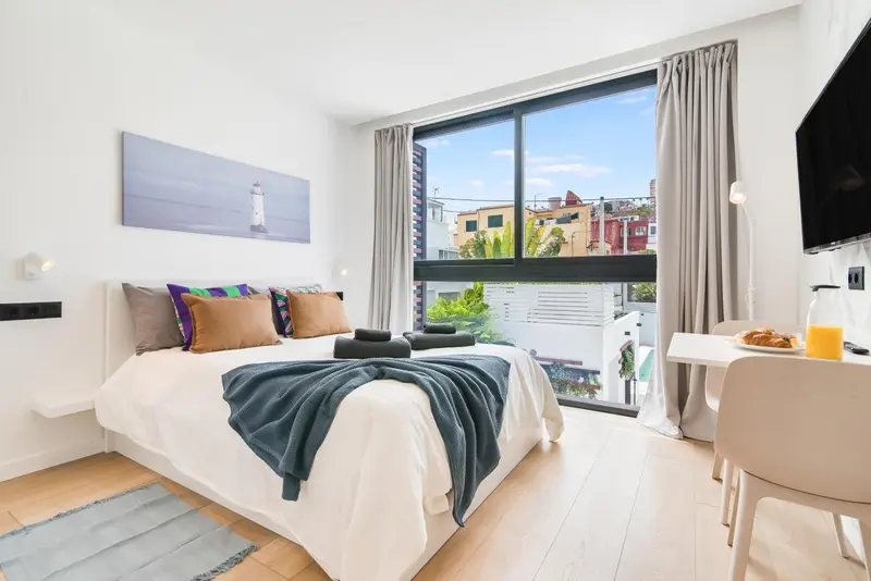 Une chambre lumineuse avec un lit fait et un coin repas près de la fenêtre.