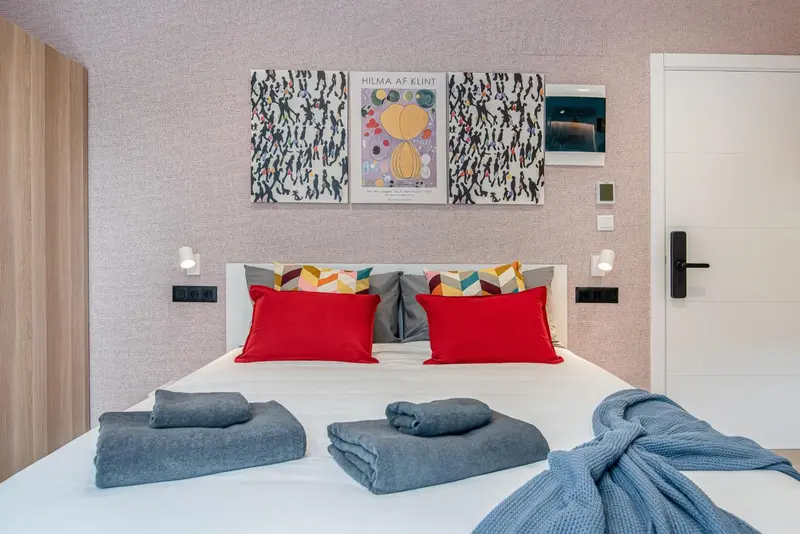 Lit double avec oreillers colorés et couvertures grises dans une chambre décorée.