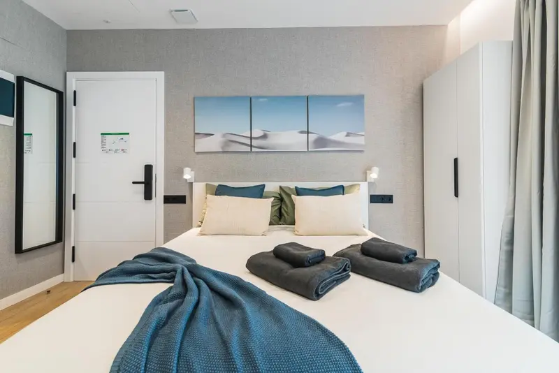 Une chambre lumineuse avec un grand lit recouvert d'une couverture bleue et de coussins.