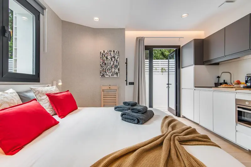 Une chambre lumineuse avec un lit fait et une kitchenette équipée.