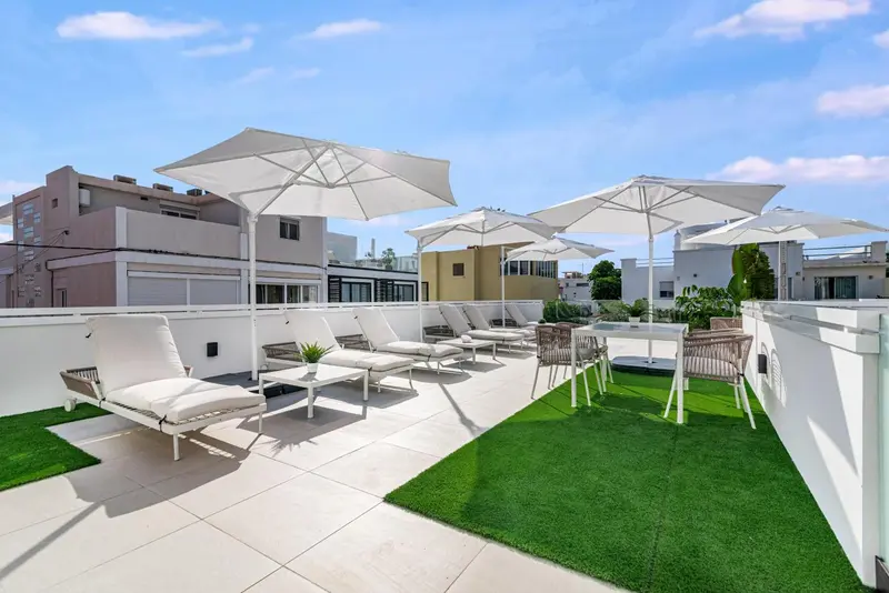 Transats blancs disposés sur une terrasse avec gazon synthétique et parasols.