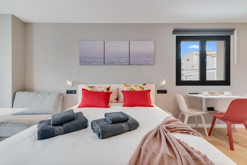 Une chambre lumineuse avec un grand lit et un coin repas près de la fenêtre.
