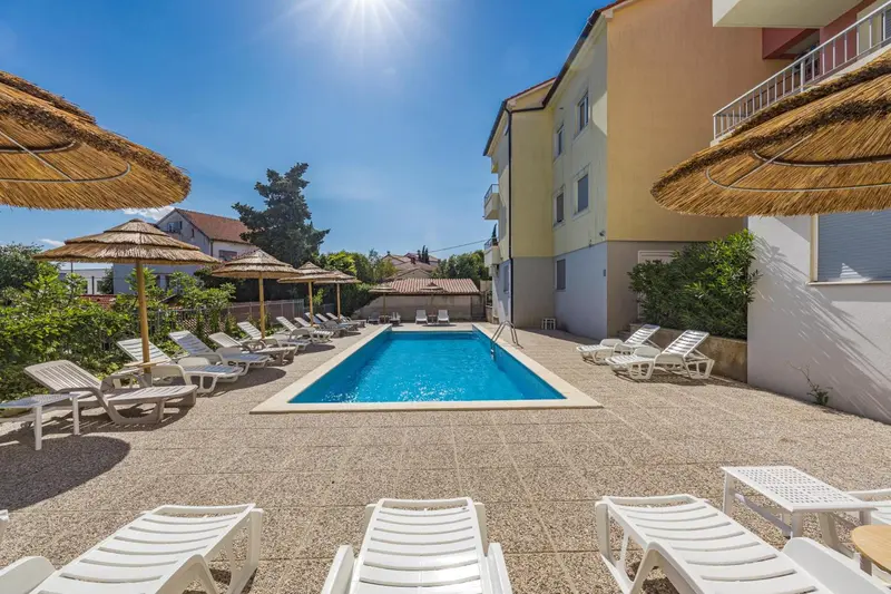 Transats blancs disposés autour d'une piscine rectangulaire dans un jardin ensoleillé.