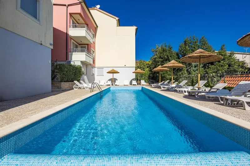 Piscine rectangulaire bleue entourée de chaises longues et de parasols.