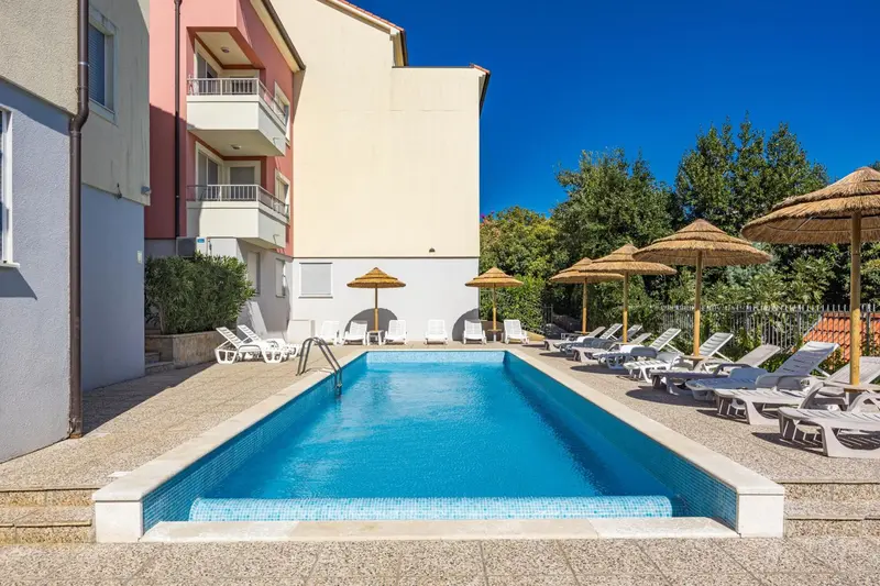 Piscine rectangulaire entourée de chaises longues et de parasols.