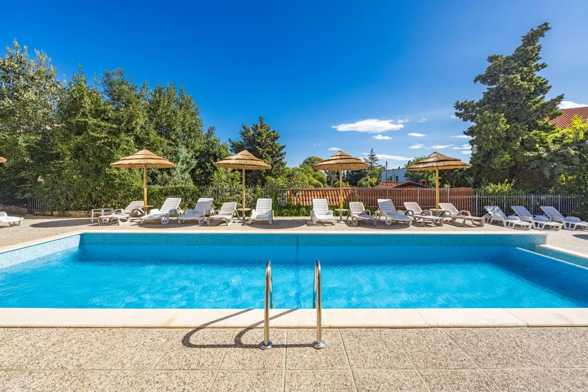 Transats et parasols ombragent une piscine rectangulaire bordée d'une terrasse carrelée.