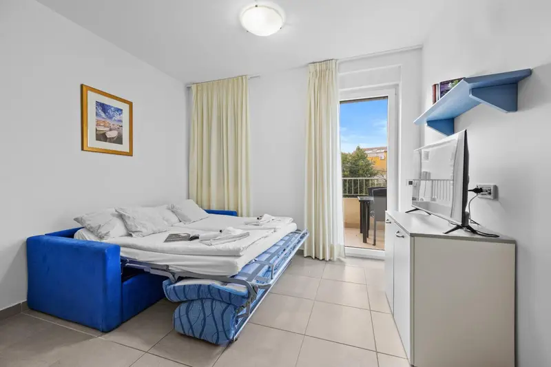 Une chambre lumineuse avec un canapé convertible et un accès à un balcon.