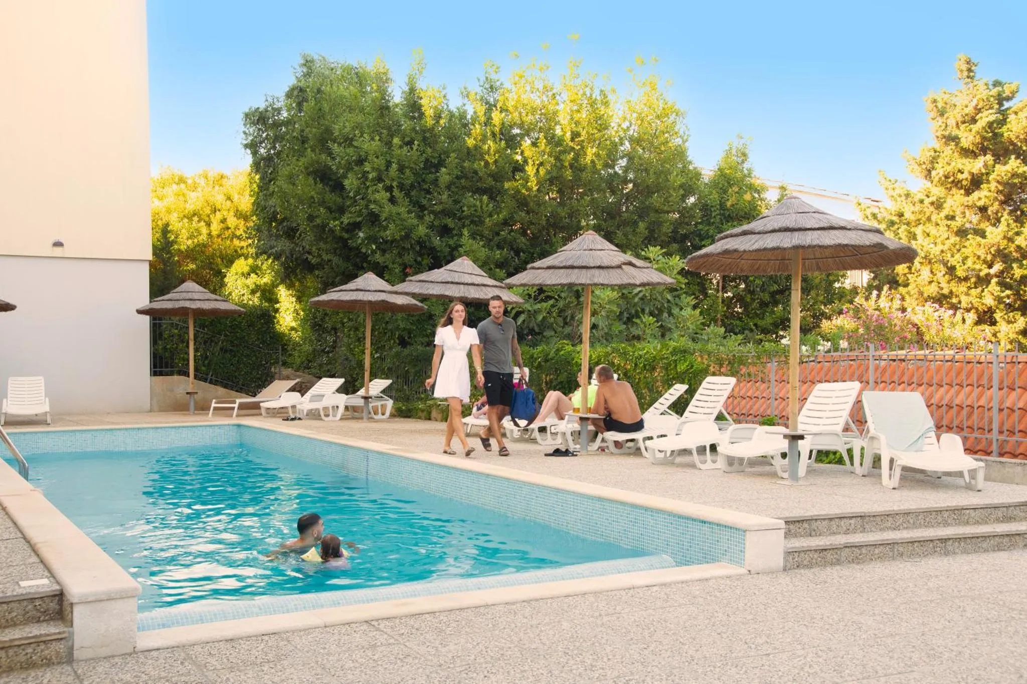 Une piscine rectangulaire bordée de transats et d'ombrelles.