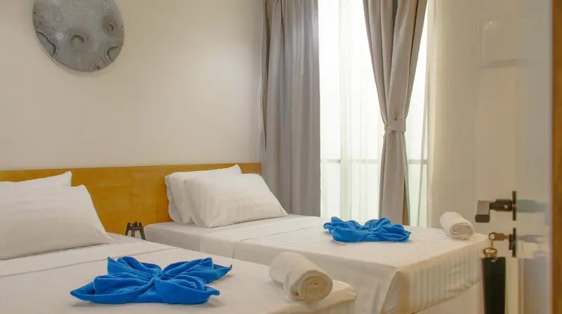 Une chambre lumineuse avec deux lits simples décorés de serviettes bleues.