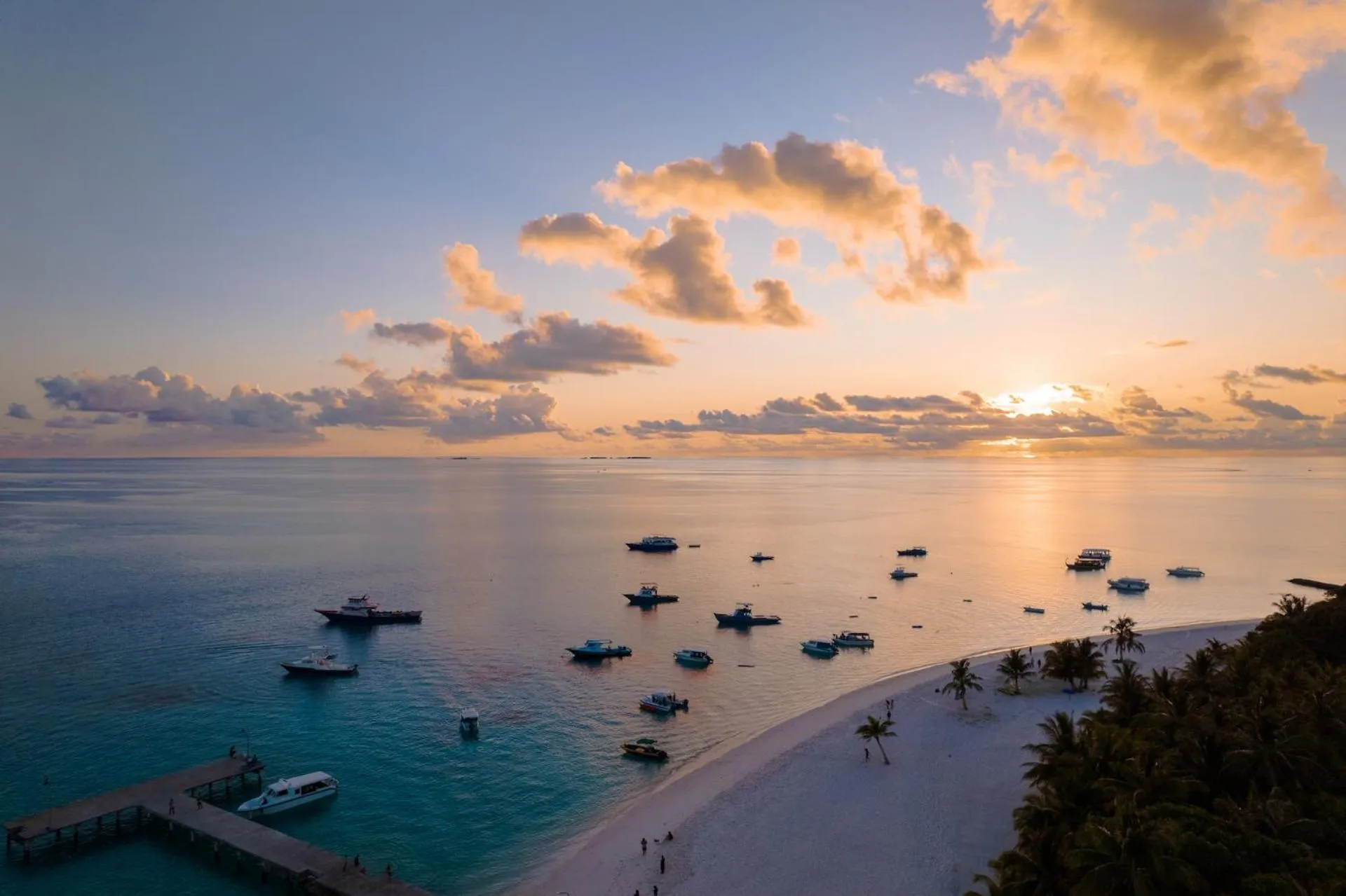 Ciel nuageux au coucher du soleil sur une mer calme et une plage de sable blanc.
