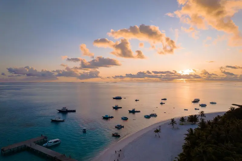 Ciel nuageux au coucher du soleil sur une mer calme et une plage de sable blanc.