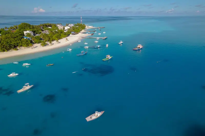 Vue aérienne d'une île tropicale avec une plage et des bateaux dans une eau turquoise.